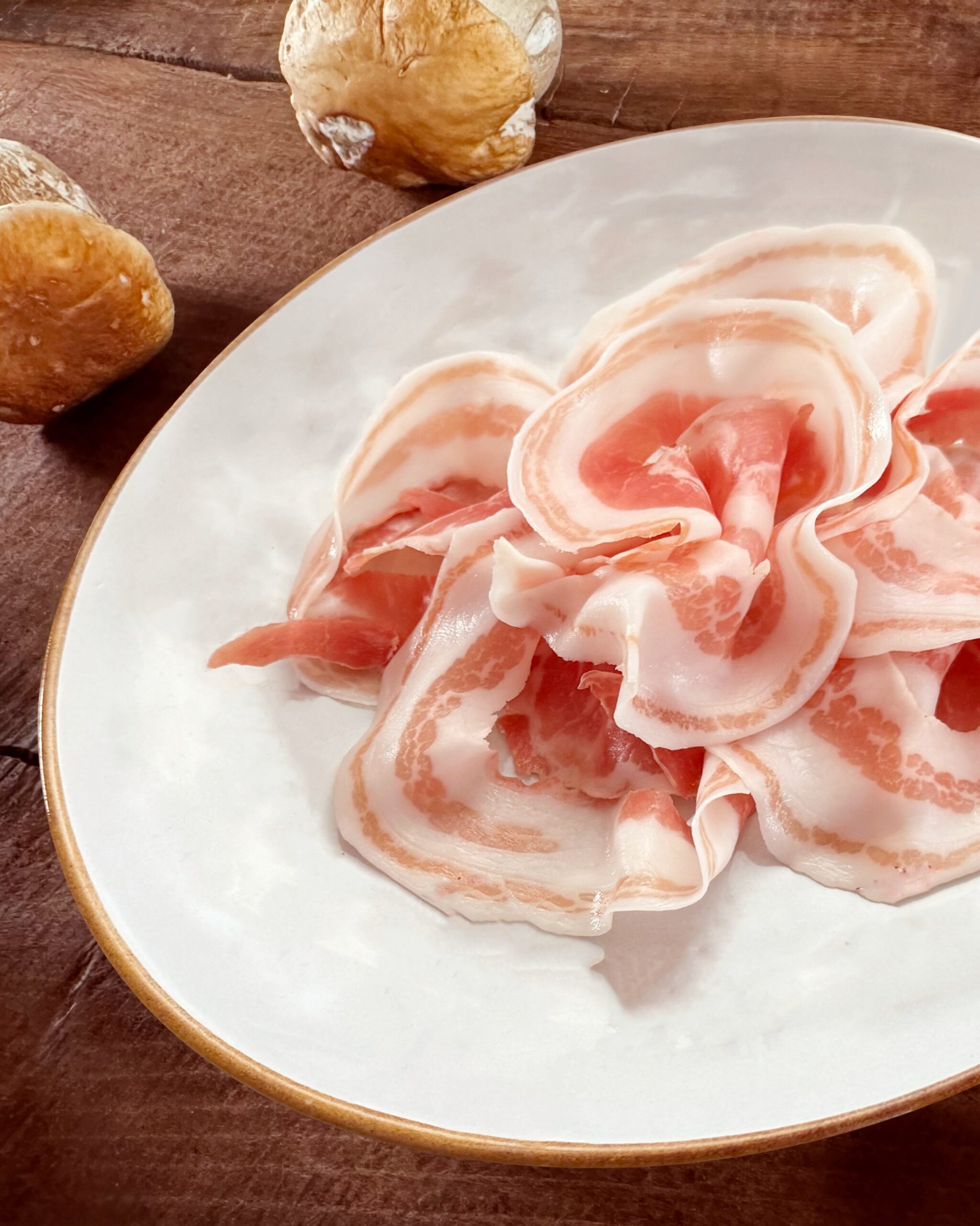 Prosciuttificio San Nicola DOP, Prospettiva Pancetta e Porcini 2 Piatto di Pancetta Piacentina con due porcini sul lato sinistro in alto.
