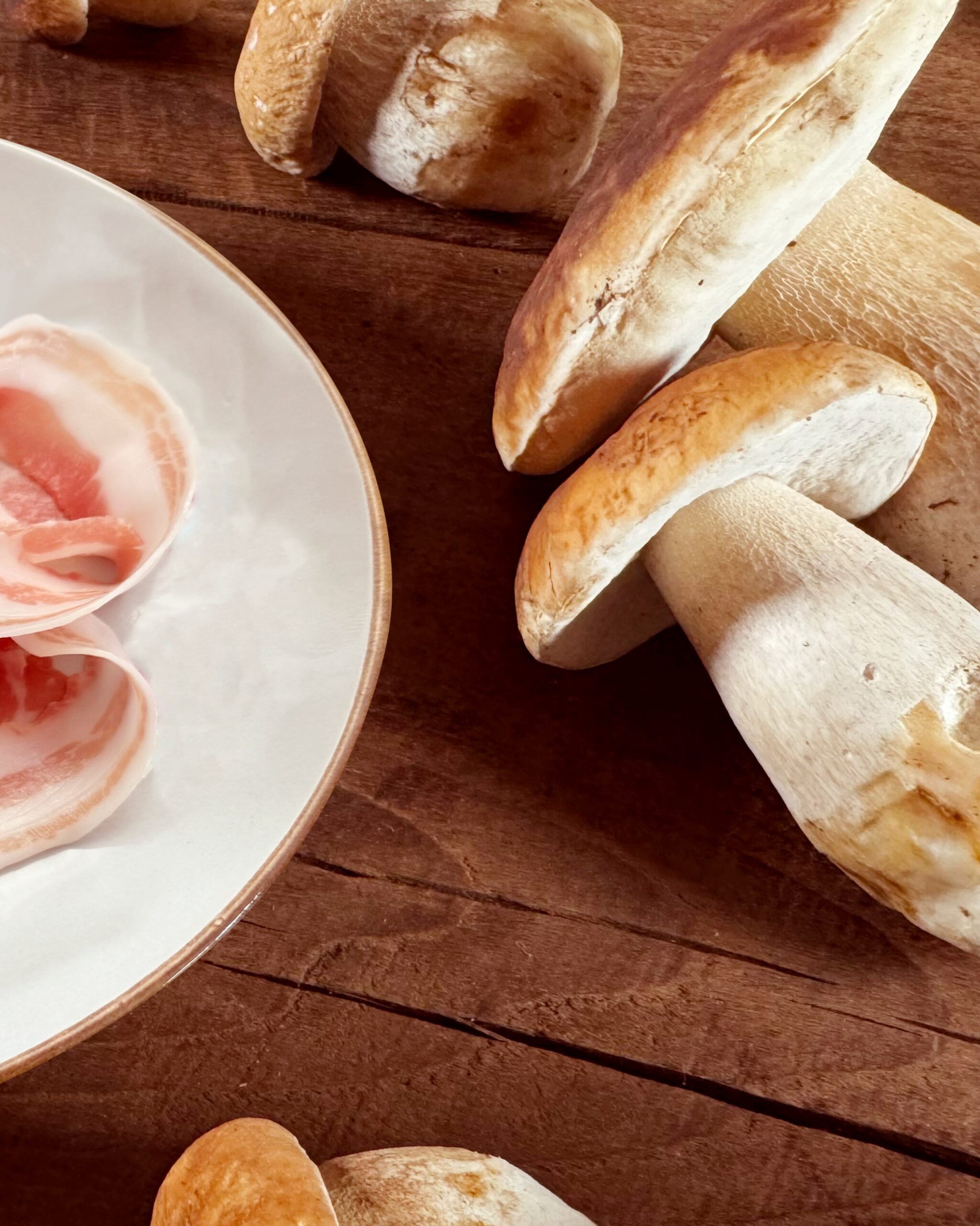 Prosciuttificio San Nicola DOP, Prospettiva Pancetta e Porcini 3 Parte di un piatto di Pancetta Piacentina e grossi funghi porcini sul lato destro.