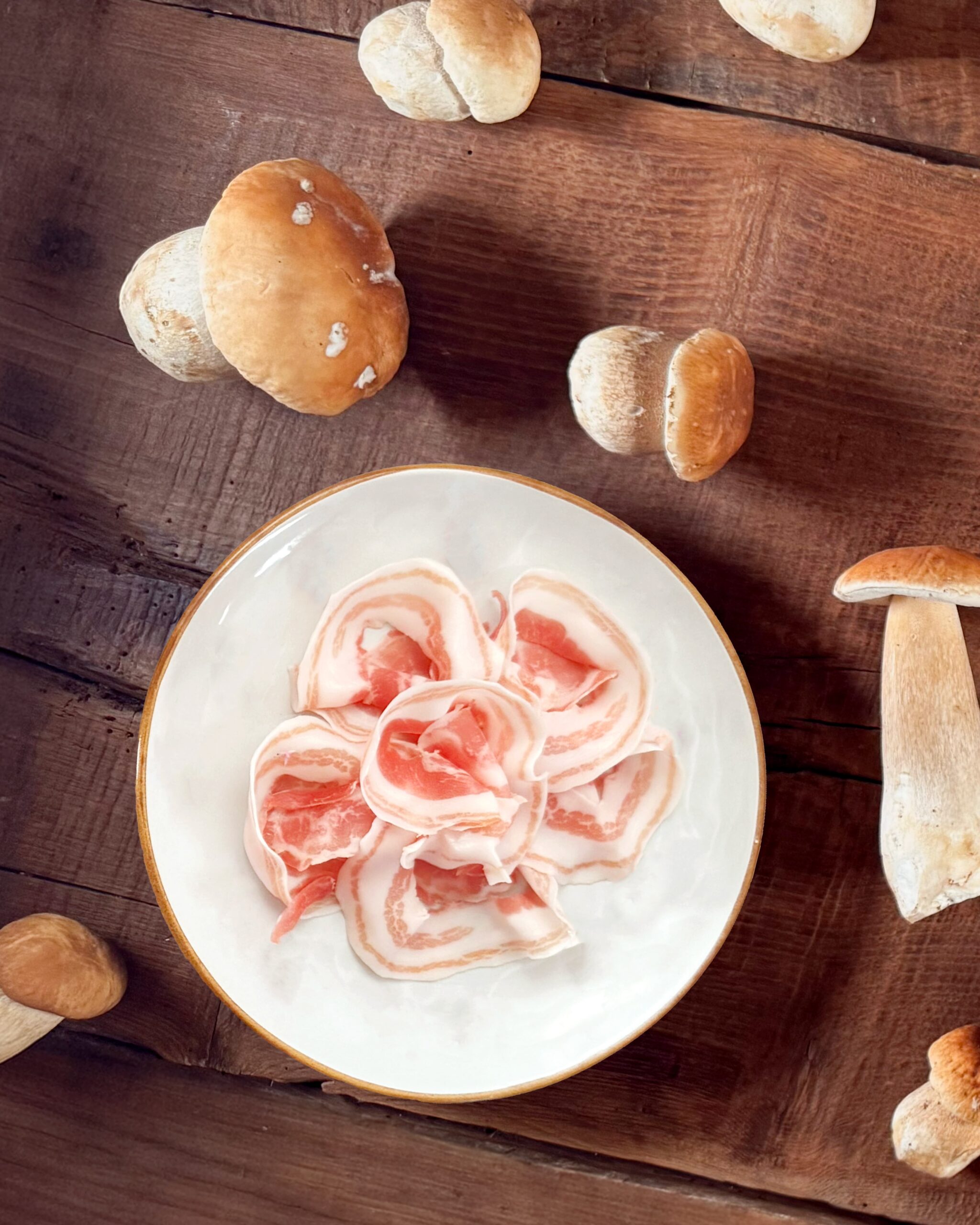 Piatto di Pancetta San Nicola DOP circondato da porcini.